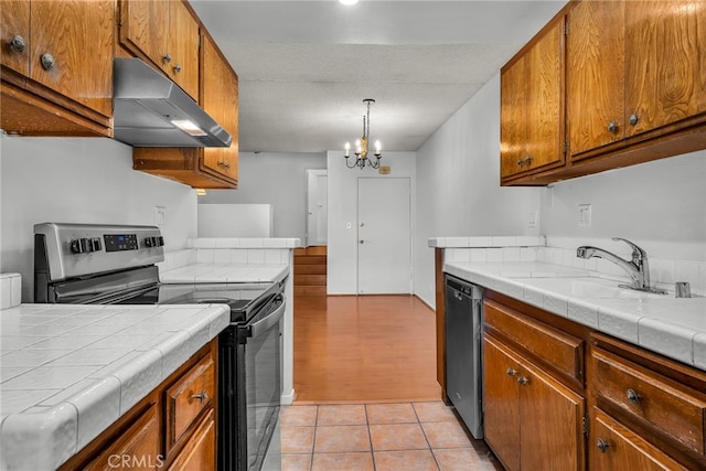 kitchen featuring stainless steel appliances, tile counters, a chandelier, and light tile patterned floors