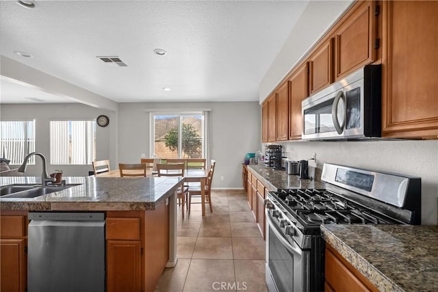 kitchen featuring brown cabinets, light tile patterned floors, visible vents, appliances with stainless steel finishes, and a sink