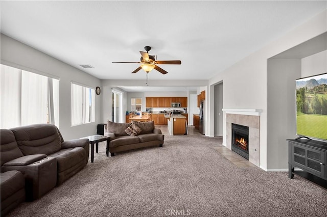 living area with a ceiling fan, visible vents, a tiled fireplace, and light colored carpet