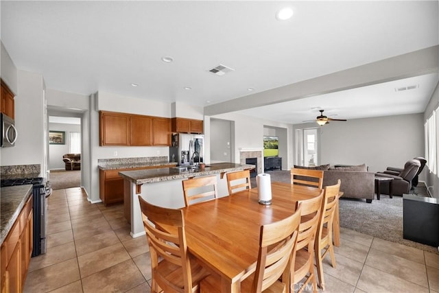 dining area with ceiling fan, visible vents, a fireplace, and light tile patterned flooring