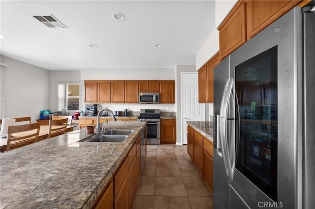 kitchen featuring a sink, visible vents, appliances with stainless steel finishes, tile counters, and brown cabinetry