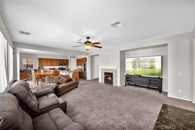 living room featuring carpet floors, a tiled fireplace, visible vents, and baseboards