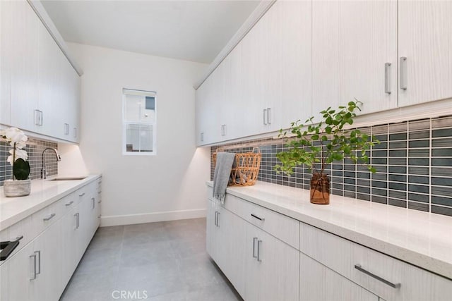 kitchen with tasteful backsplash, white cabinetry, light stone countertops, and sink