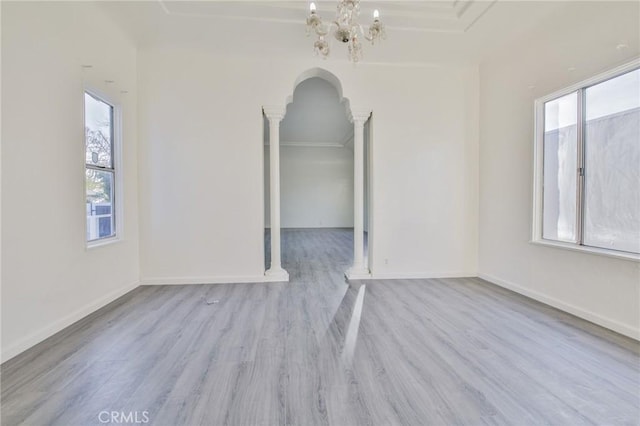 empty room featuring an inviting chandelier, ornamental molding, light hardwood / wood-style floors, and decorative columns