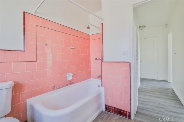 bathroom featuring wood-type flooring, toilet, tiled shower / bath combo, and tile walls