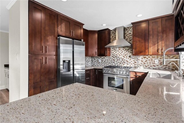 kitchen with appliances with stainless steel finishes, backsplash, ornamental molding, light stone countertops, and wall chimney range hood