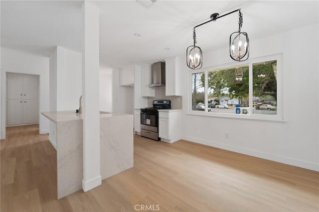 kitchen featuring pendant lighting, wall chimney range hood, stainless steel gas range, light hardwood / wood-style flooring, and white cabinetry