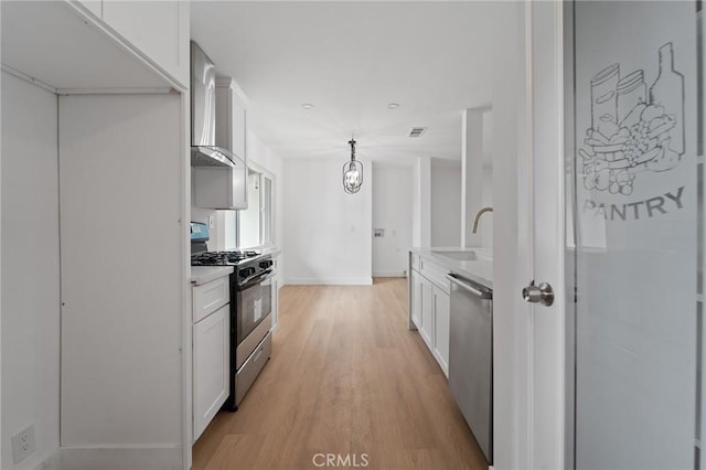 kitchen featuring pendant lighting, sink, white cabinetry, stainless steel appliances, and wall chimney exhaust hood