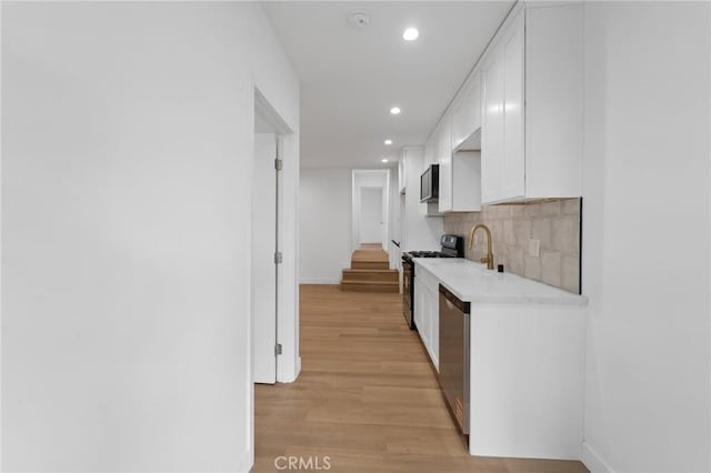 kitchen featuring sink, stainless steel appliances, light hardwood / wood-style floors, white cabinets, and decorative backsplash