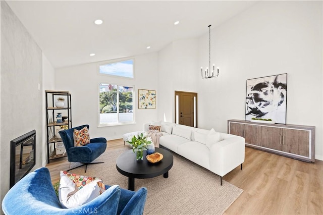 living area featuring a glass covered fireplace, an inviting chandelier, light wood-style floors, high vaulted ceiling, and recessed lighting