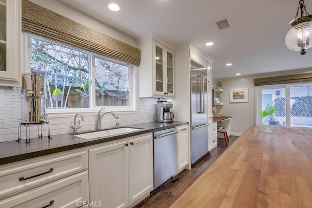 kitchen featuring sink, dark wood-type flooring, appliances with stainless steel finishes, white cabinets, and decorative light fixtures