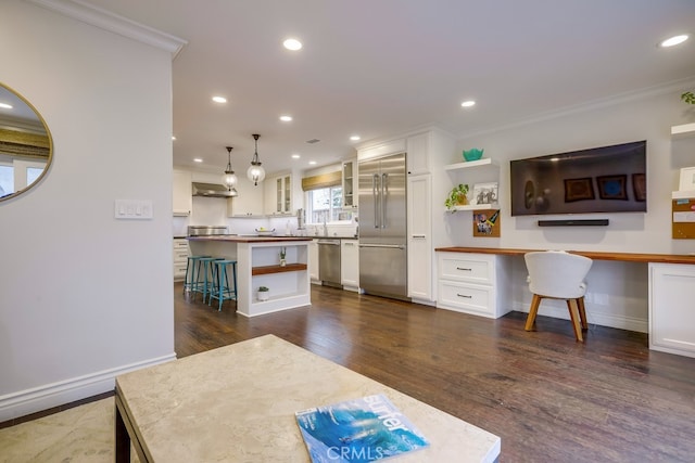 kitchen with stainless steel appliances, built in desk, white cabinets, and decorative light fixtures