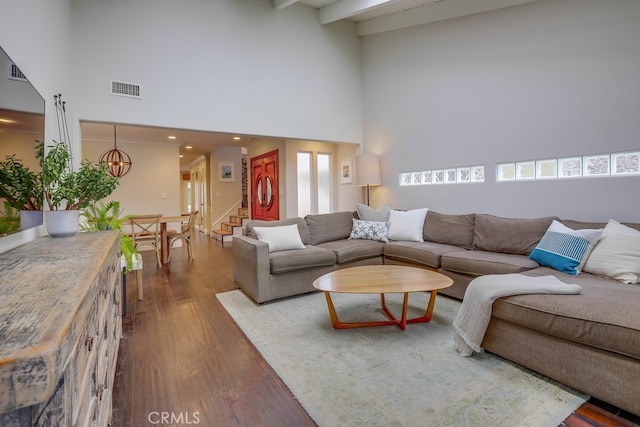 living room featuring dark hardwood / wood-style flooring, beamed ceiling, a chandelier, and a high ceiling