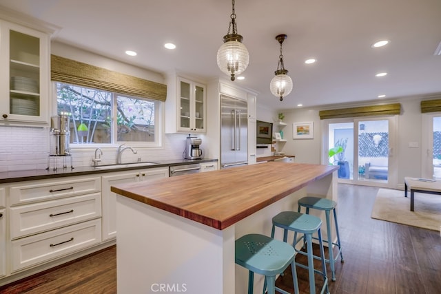 kitchen with a kitchen island, pendant lighting, butcher block countertops, white cabinetry, and sink