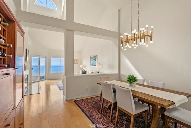 dining room featuring high vaulted ceiling, a chandelier, a water view, and light wood-style flooring