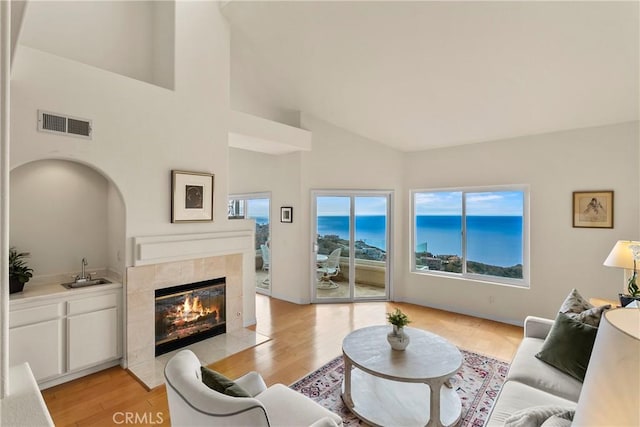 living area featuring high vaulted ceiling, a fireplace, a water view, visible vents, and light wood-style floors