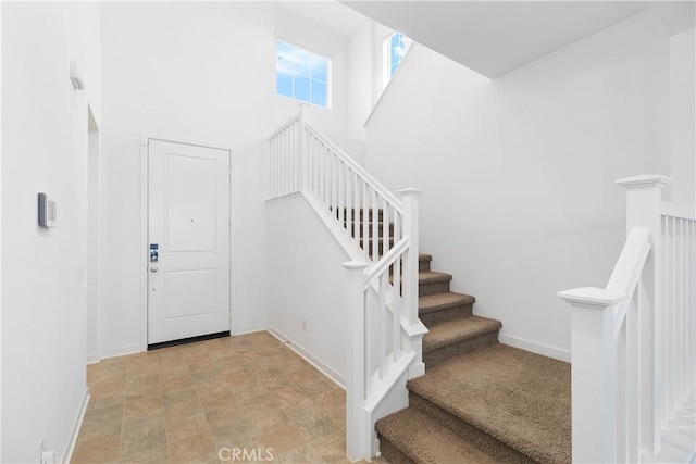 staircase featuring a high ceiling, baseboards, and stone finish flooring