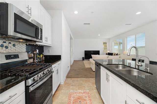 kitchen with a sink, dark stone countertops, tasteful backsplash, white cabinetry, and stainless steel appliances