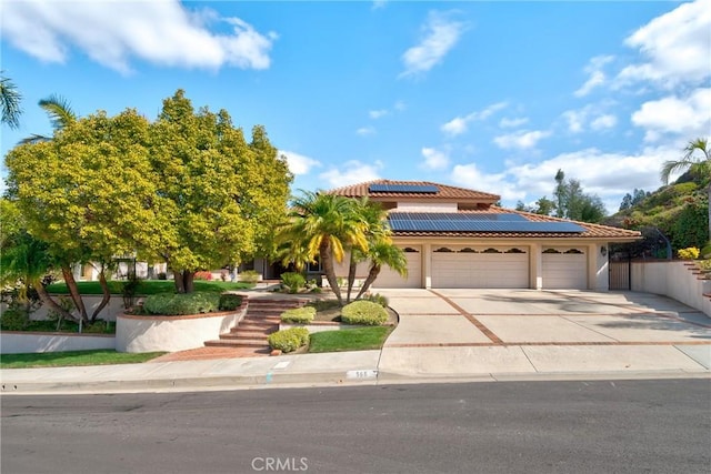 mediterranean / spanish house with stucco siding, driveway, roof mounted solar panels, an attached garage, and a tiled roof