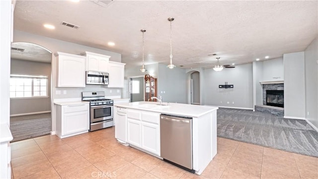 kitchen with stainless steel appliances, a center island with sink, white cabinets, and decorative light fixtures