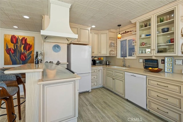 kitchen featuring pendant lighting, sink, white appliances, custom range hood, and cream cabinetry