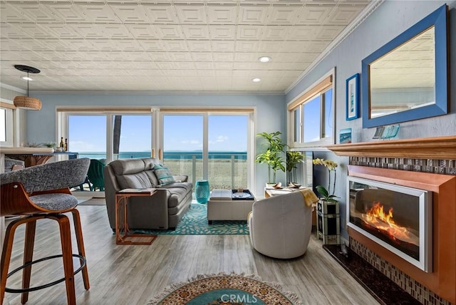 living area featuring an ornate ceiling, crown molding, a glass covered fireplace, plenty of natural light, and a water view