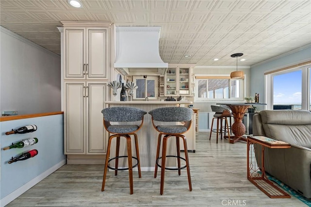 kitchen featuring pendant lighting, ornamental molding, light hardwood / wood-style floors, custom exhaust hood, and cream cabinetry