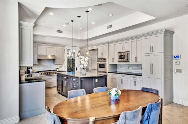 kitchen featuring pendant lighting, gray cabinets, stainless steel appliances, a kitchen island, and dark stone counters