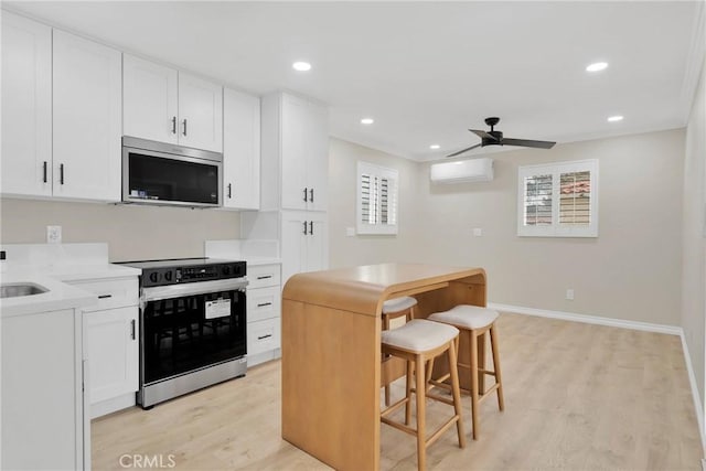 kitchen with a breakfast bar, appliances with stainless steel finishes, white cabinetry, light hardwood / wood-style floors, and an AC wall unit