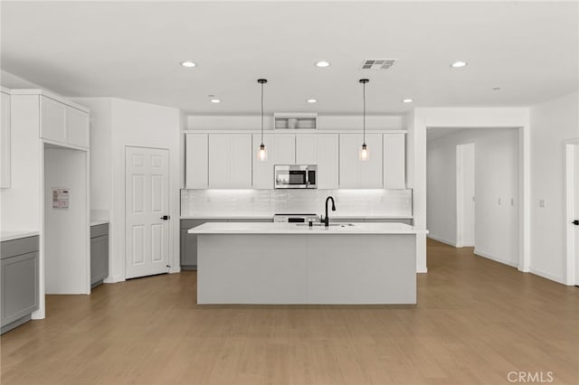 kitchen with a kitchen island with sink, stainless steel microwave, visible vents, and light wood-type flooring