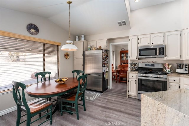 kitchen with appliances with stainless steel finishes, lofted ceiling, white cabinets, hanging light fixtures, and hardwood / wood-style flooring