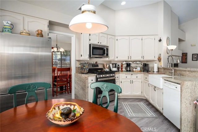 kitchen with white cabinetry, stainless steel appliances, light stone countertops, and hanging light fixtures