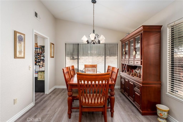 dining space with an inviting chandelier, lofted ceiling, light hardwood / wood-style floors, and plenty of natural light