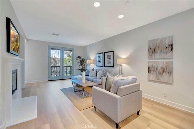 living room featuring light wood-type flooring, a glass covered fireplace, visible vents, and baseboards