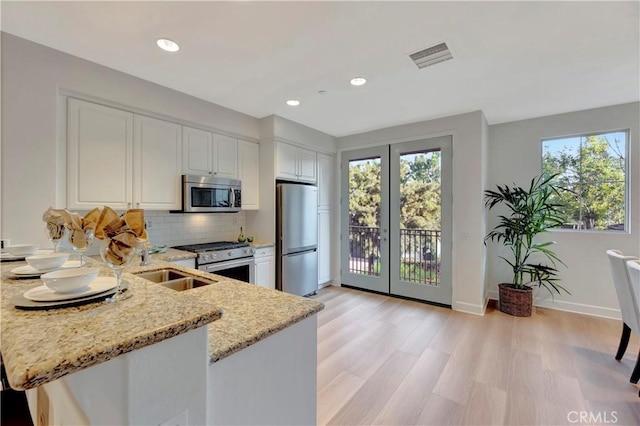 kitchen with stainless steel appliances, white cabinets, a peninsula, and light stone counters