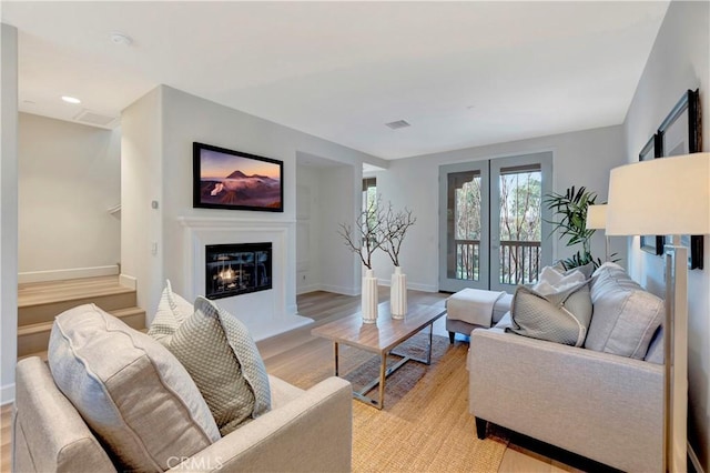 living room featuring light wood-style flooring, visible vents, baseboards, and a glass covered fireplace