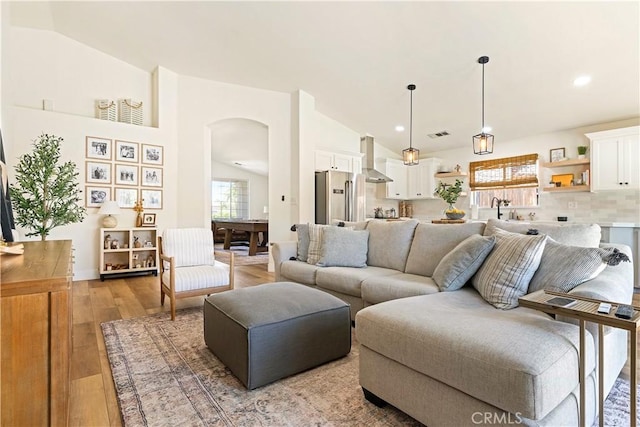 living room featuring vaulted ceiling, sink, and light hardwood / wood-style flooring