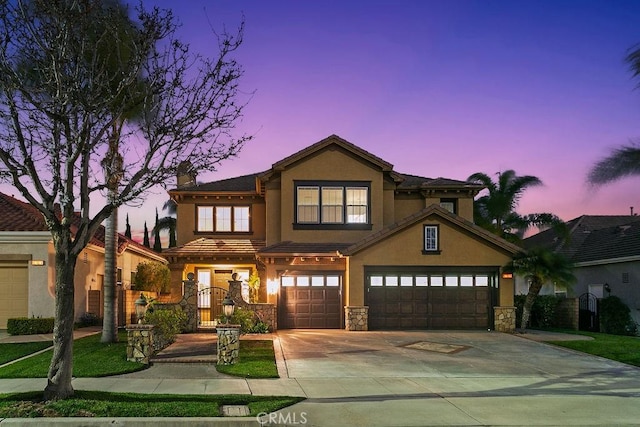 view of front of house with concrete driveway, stone siding, an attached garage, a gate, and stucco siding