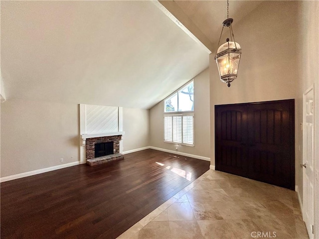 entrance foyer with wood finished floors, baseboards, high vaulted ceiling, an inviting chandelier, and a brick fireplace