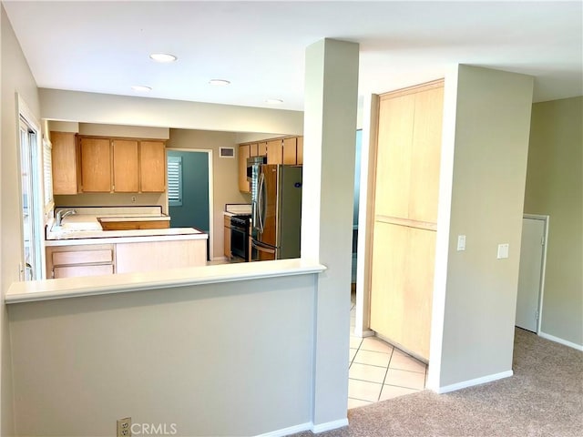 kitchen featuring baseboards, light carpet, range with gas stovetop, a peninsula, and freestanding refrigerator