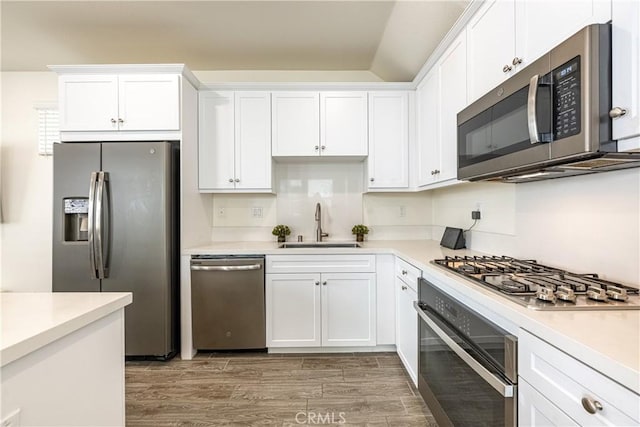 kitchen with stainless steel appliances, white cabinetry, sink, and hardwood / wood-style floors