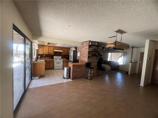 kitchen with sink, gas range gas stove, a textured ceiling, kitchen peninsula, and light hardwood / wood-style floors