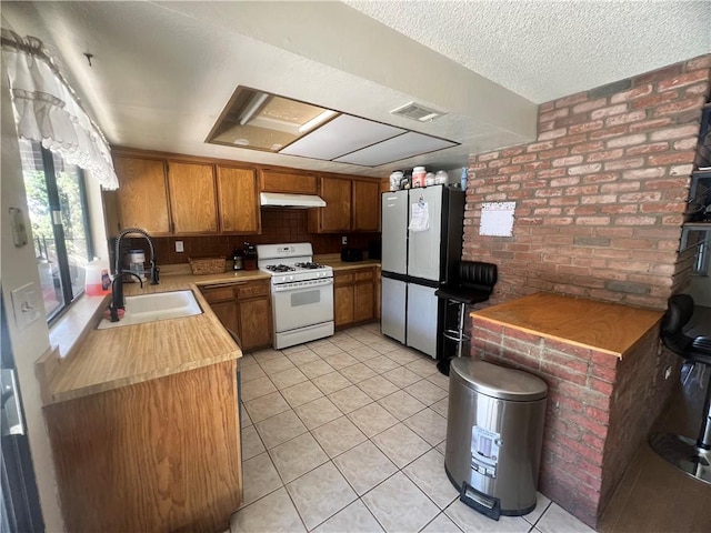 kitchen with light tile patterned floors, gas range gas stove, stainless steel refrigerator, a textured ceiling, and brick wall