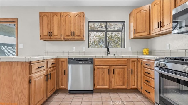 kitchen with appliances with stainless steel finishes, tile counters, a sink, and light tile patterned floors