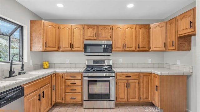 kitchen featuring tile counters, stainless steel appliances, a sink, and recessed lighting