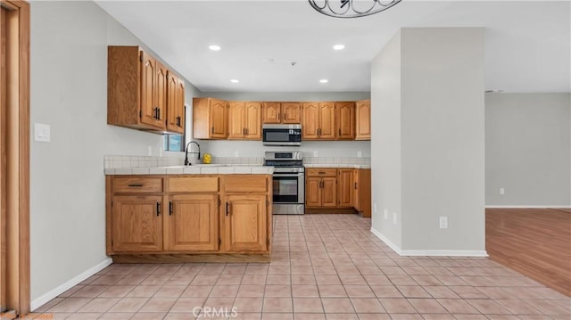 kitchen featuring tile counters, recessed lighting, appliances with stainless steel finishes, a sink, and baseboards