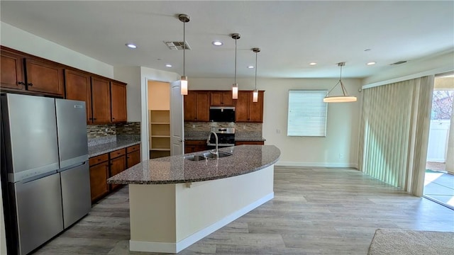 kitchen with sink, tasteful backsplash, hanging light fixtures, appliances with stainless steel finishes, and a kitchen island with sink