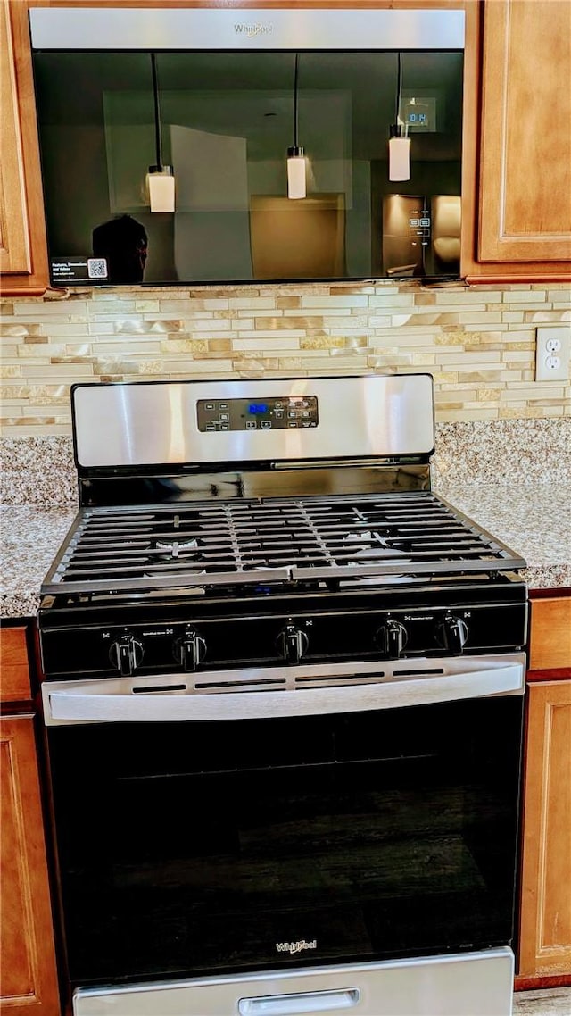 details featuring tasteful backsplash, light stone countertops, stainless steel range with gas cooktop, and hanging light fixtures