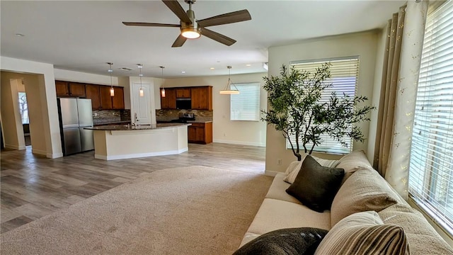 kitchen with appliances with stainless steel finishes, an island with sink, pendant lighting, ceiling fan, and backsplash