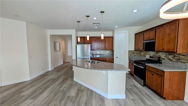 kitchen featuring appliances with stainless steel finishes, pendant lighting, tasteful backsplash, sink, and a center island with sink